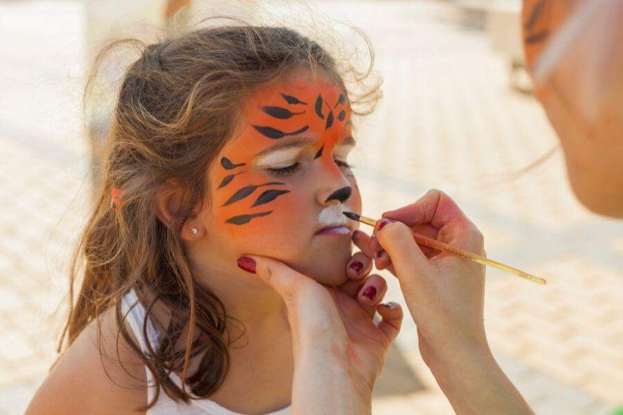 kobieta malujaca dziewczynce na twarzy makijaz tygrysa